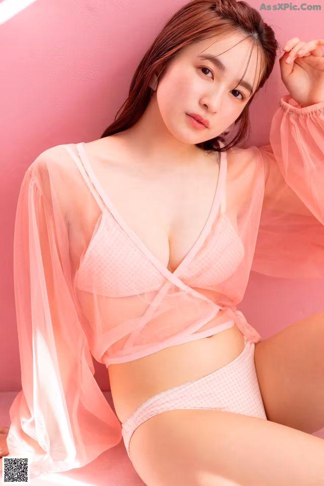 A woman in a pink lingerie sitting on a pink surface.