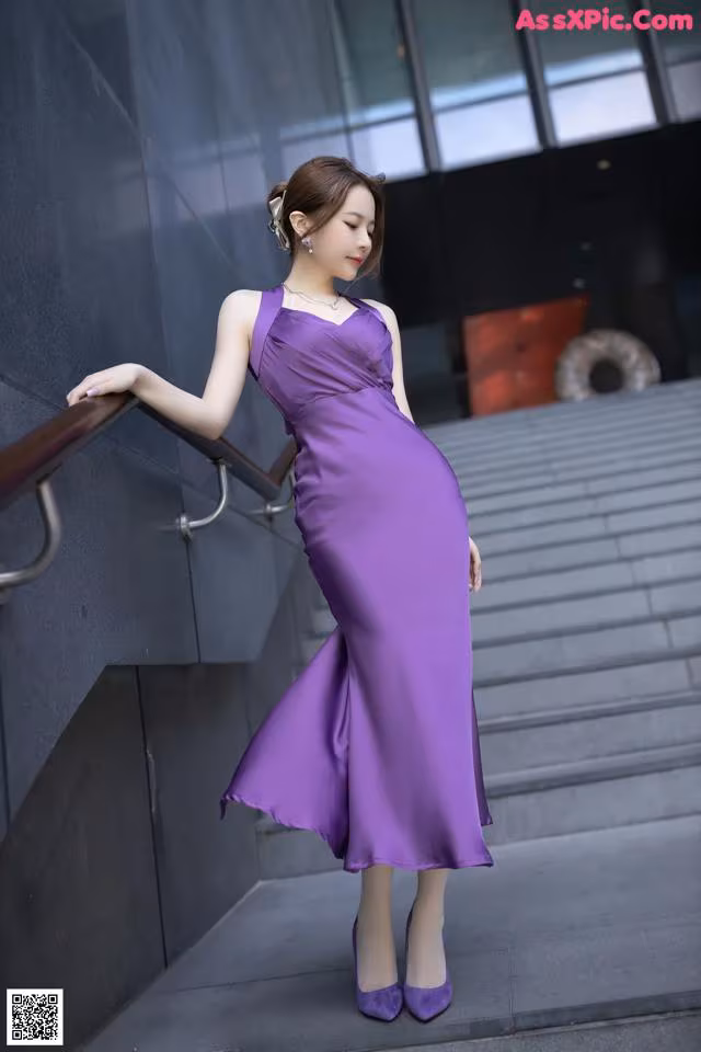 A woman in a purple dress leaning against a wall.