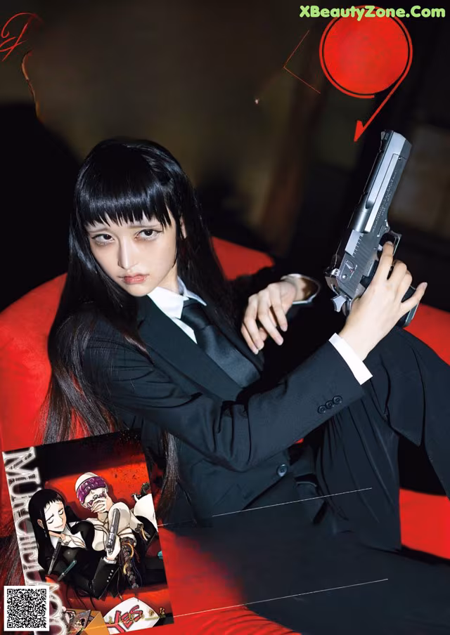 A woman in a suit holding a gun on a red couch.