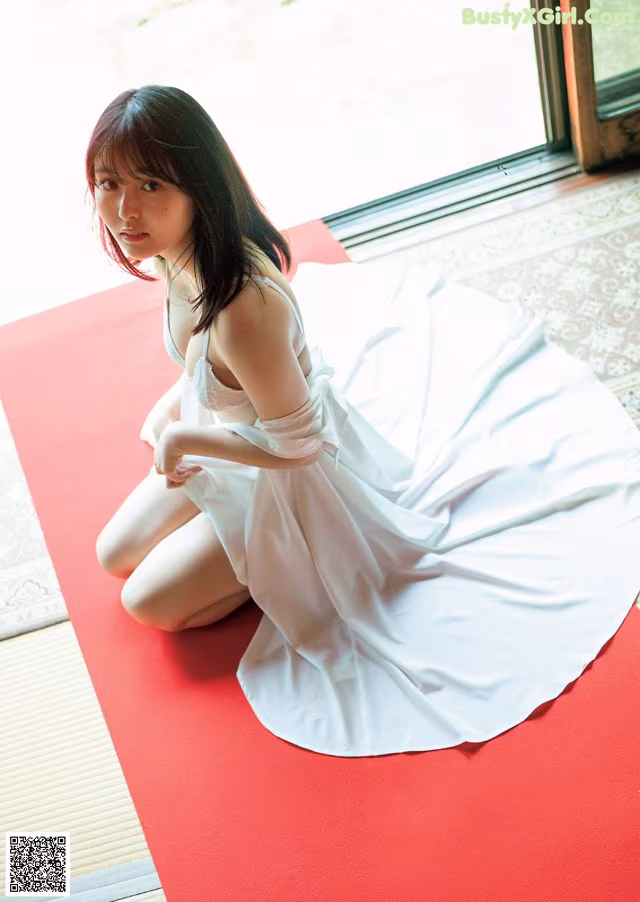 A woman in a white dress sitting on a red mat.