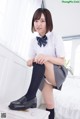 A woman in a school uniform sitting on a bed.