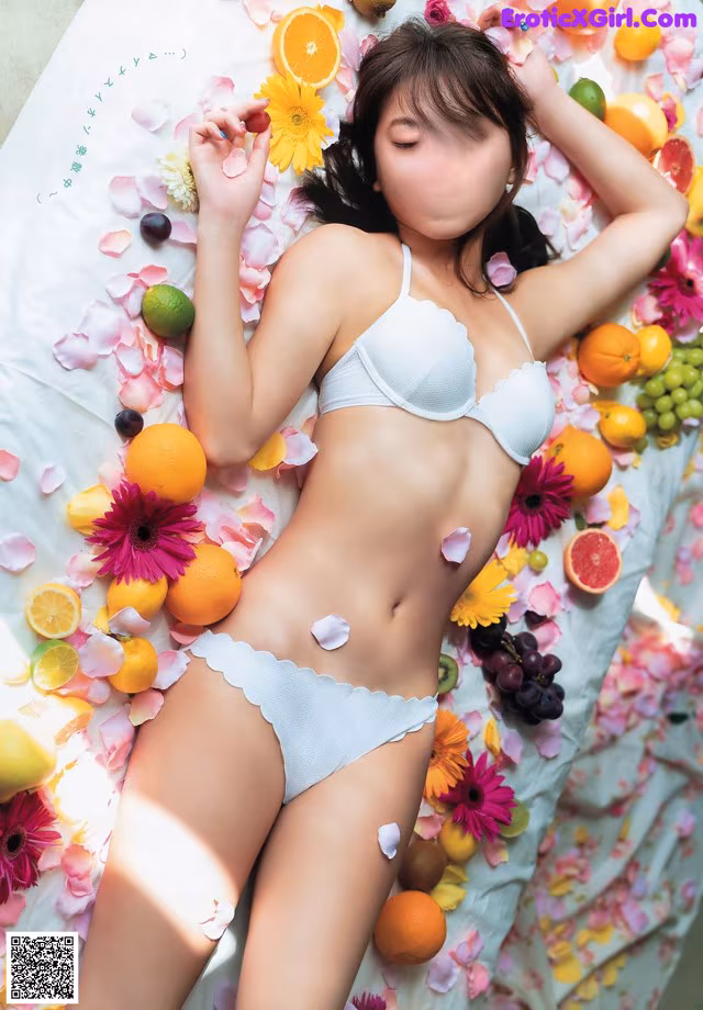 A woman laying on a bed covered in fruit and flowers.