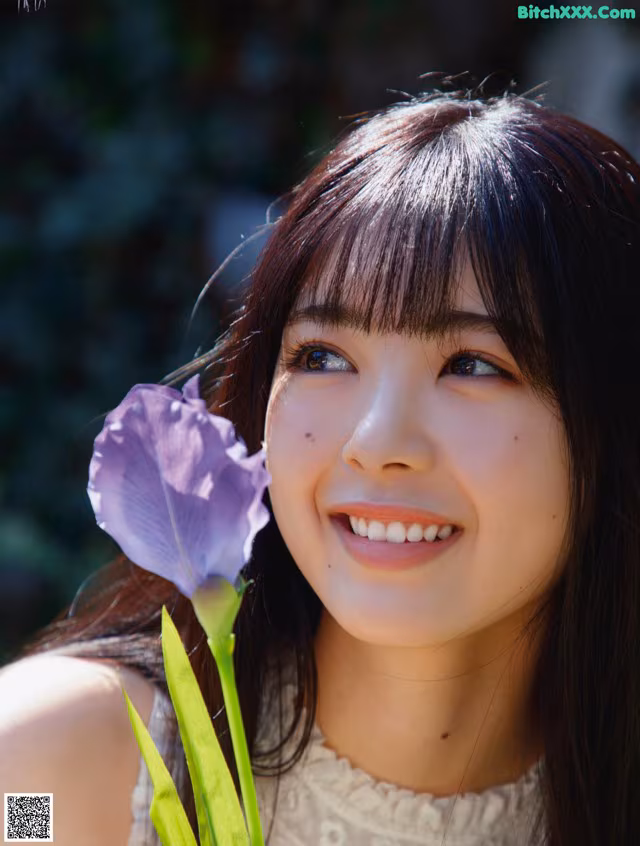A young woman holding a purple flower in her hand.