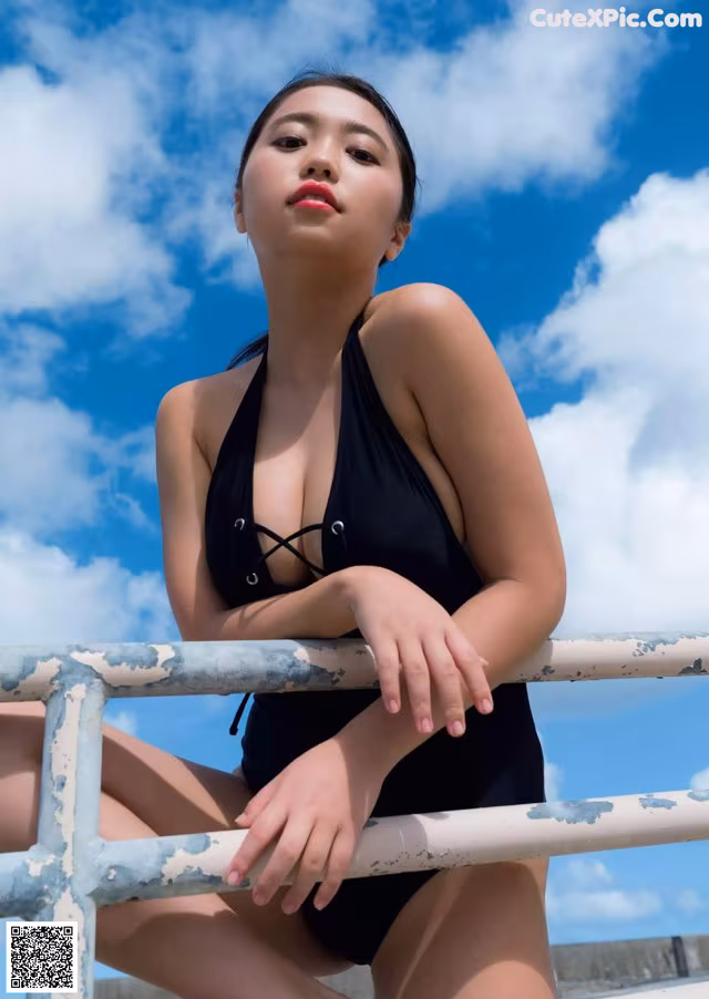 A woman in a black bathing suit sitting on a railing.