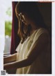 A woman in a white shirt is looking out a window.