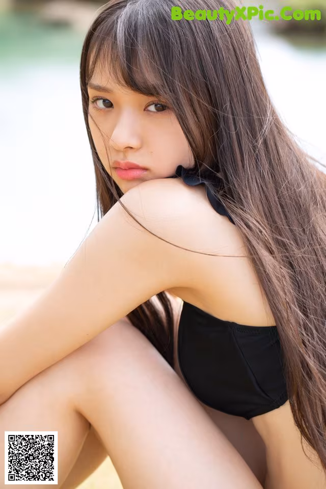 A woman in a black bikini sitting on the ground.