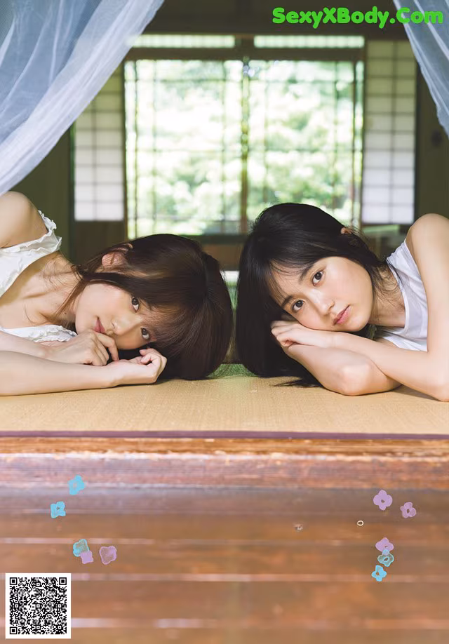A couple of young women laying on top of a bed.