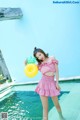 A woman in a pink dress holding a yellow ball in a pool.