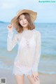 A woman in a white lace top and a straw hat on the beach.